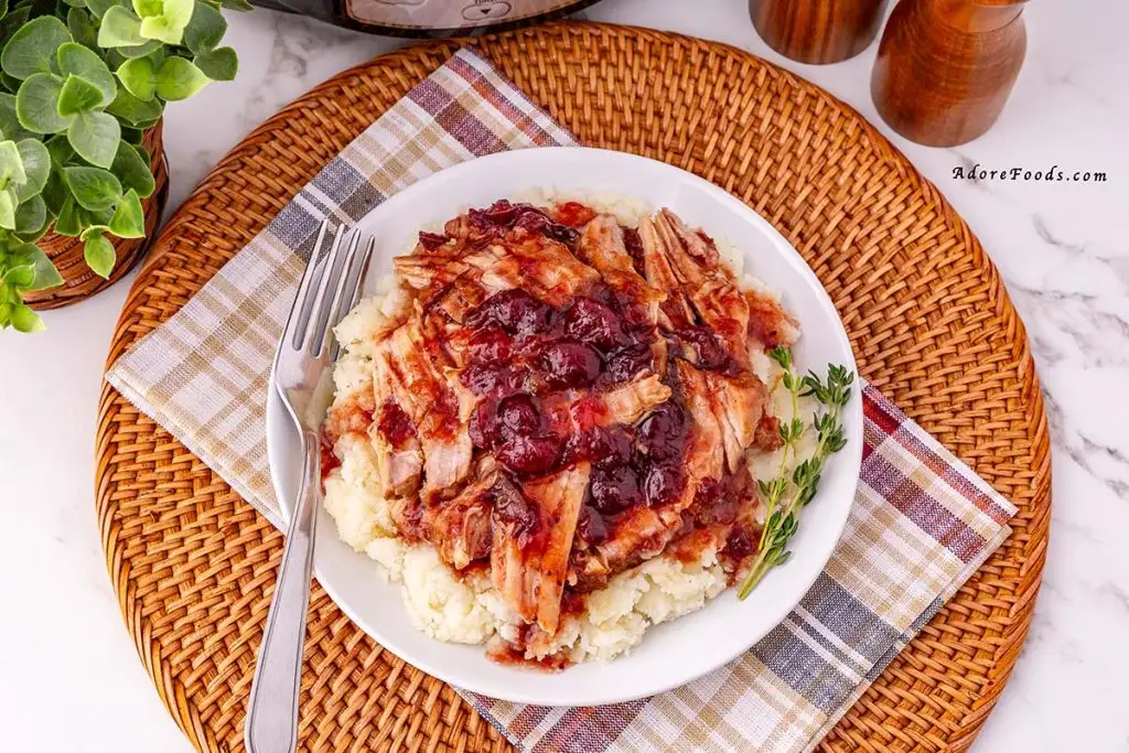 Juicy cranberry-glazed pork loin sliced and served over a bed of creamy mashed potatoes, topped with glossy cranberry pan sauce that drips down the edges, creating a rich contrast of tender pork, tart red cranberries, and fluffy golden potatoes on the plate.