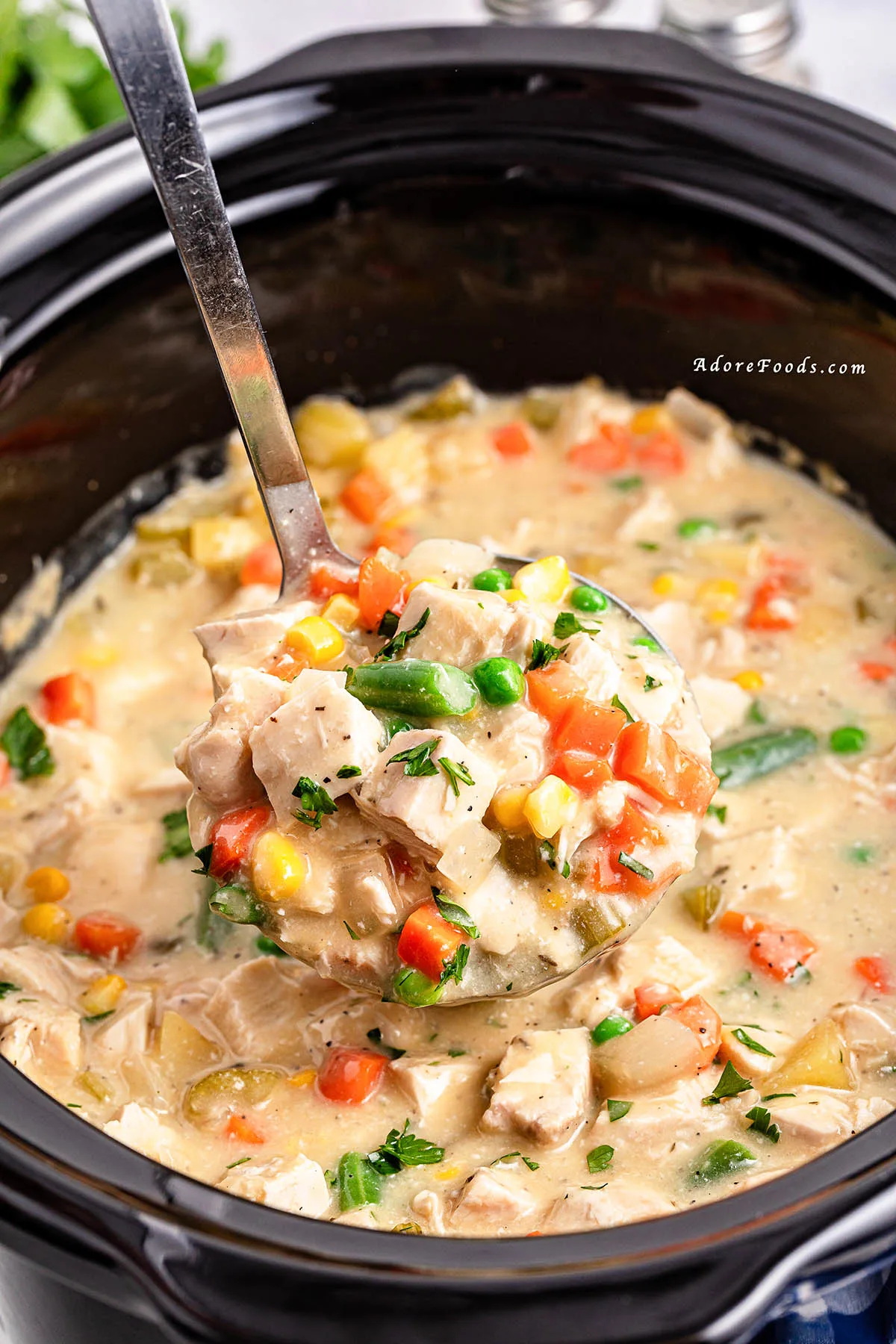 Overhead view of a creamy chicken pot pie filling cooked in a slow cooker, loaded with shredded chicken, tender potatoes, carrots, peas, and corn, served alongside golden-brown buttermilk biscuits on a plate, showcasing a hearty and comforting homemade crockpot dinner.