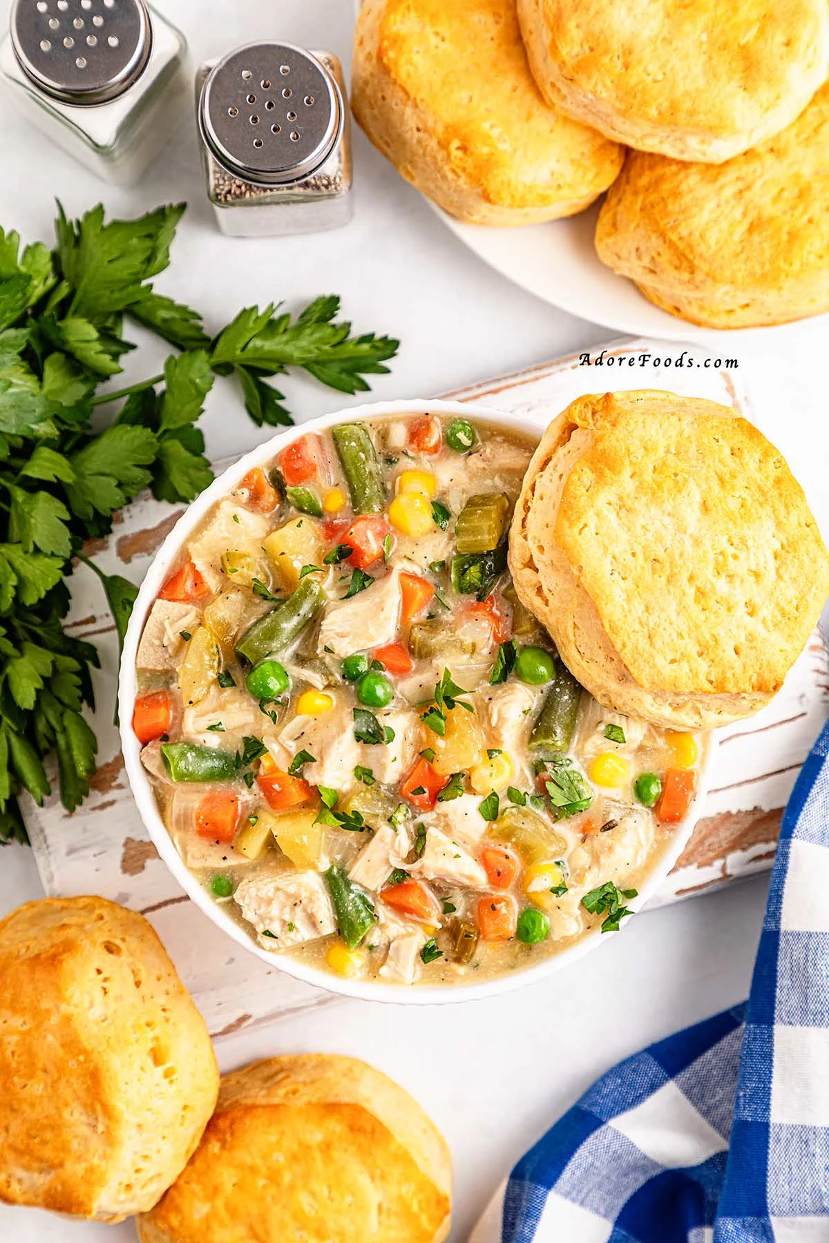 Overhead view of a creamy chicken pot pie filling cooked in a slow cooker, loaded with shredded chicken, tender potatoes, carrots, peas, and corn, served alongside golden-brown buttermilk biscuits on a plate, showcasing a hearty and comforting homemade crockpot dinner.