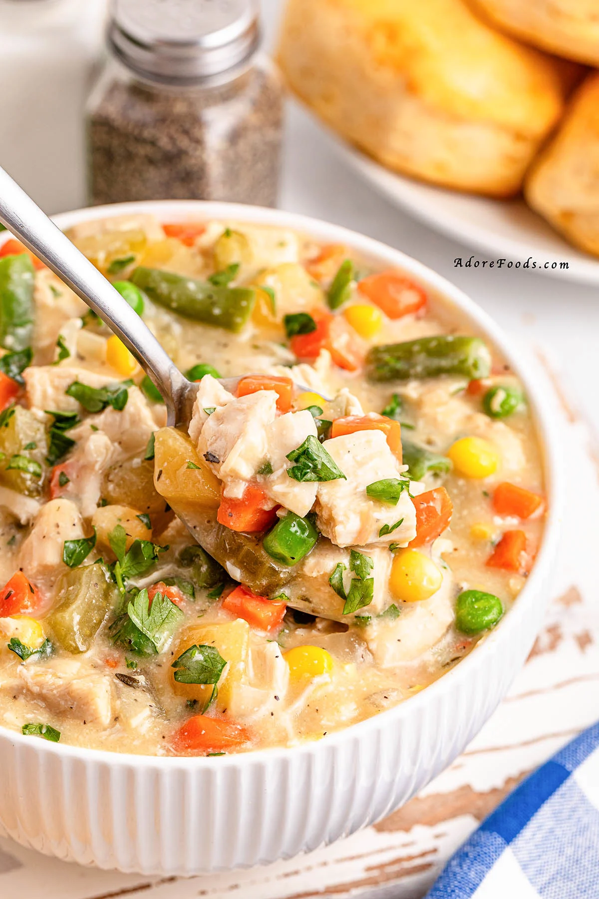 Overhead view of a creamy chicken pot pie filling cooked in a slow cooker, loaded with shredded chicken, tender potatoes, carrots, peas, and corn, served alongside golden-brown buttermilk biscuits on a plate, showcasing a hearty and comforting homemade crockpot dinner.