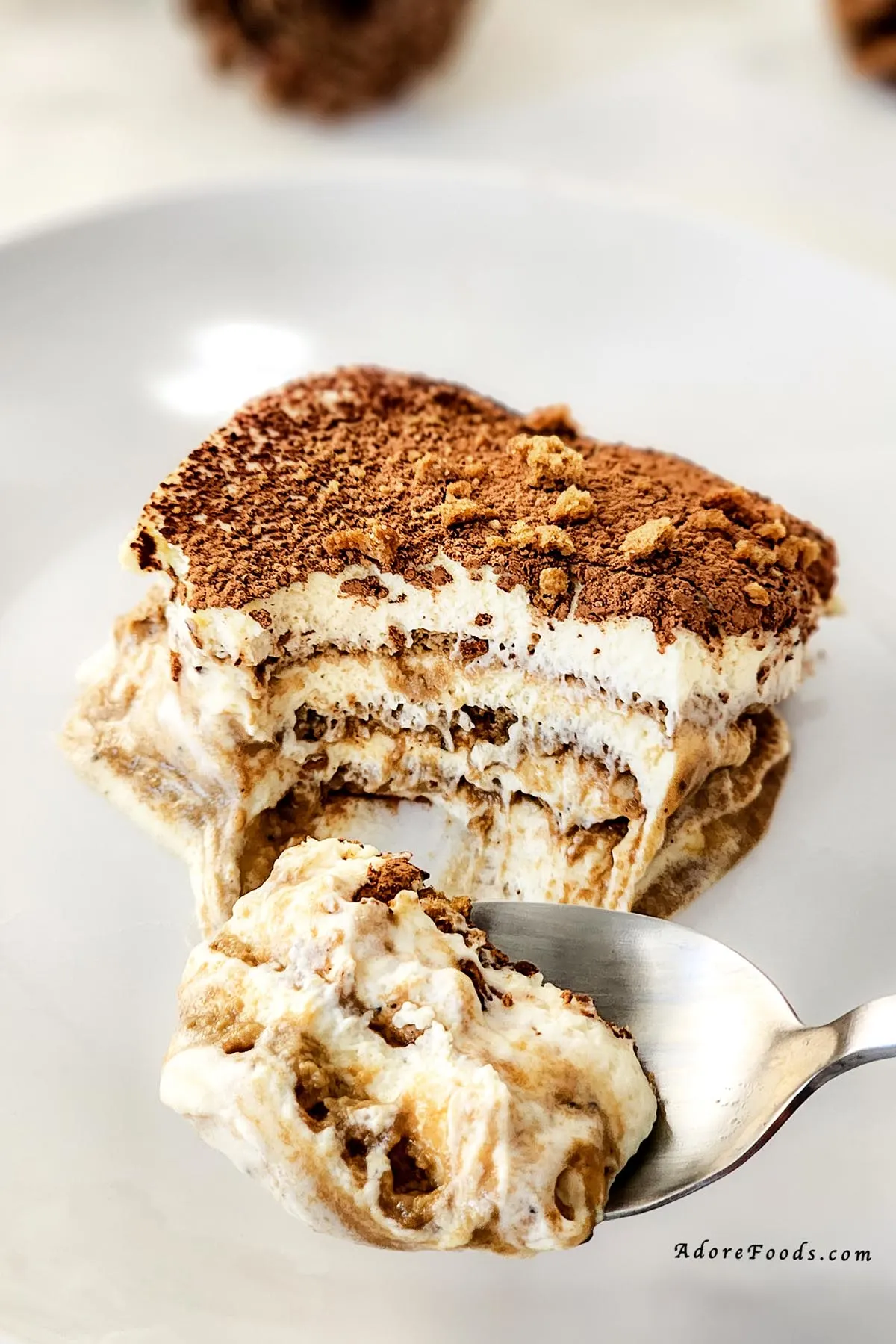 Slice of gingerbread tiramisu served on a white plate with a fork, showing distinct layers of spiced cookies, mascarpone cream, and cocoa topping, garnished with crushed gingerbread for a festive holiday dessert presentation.