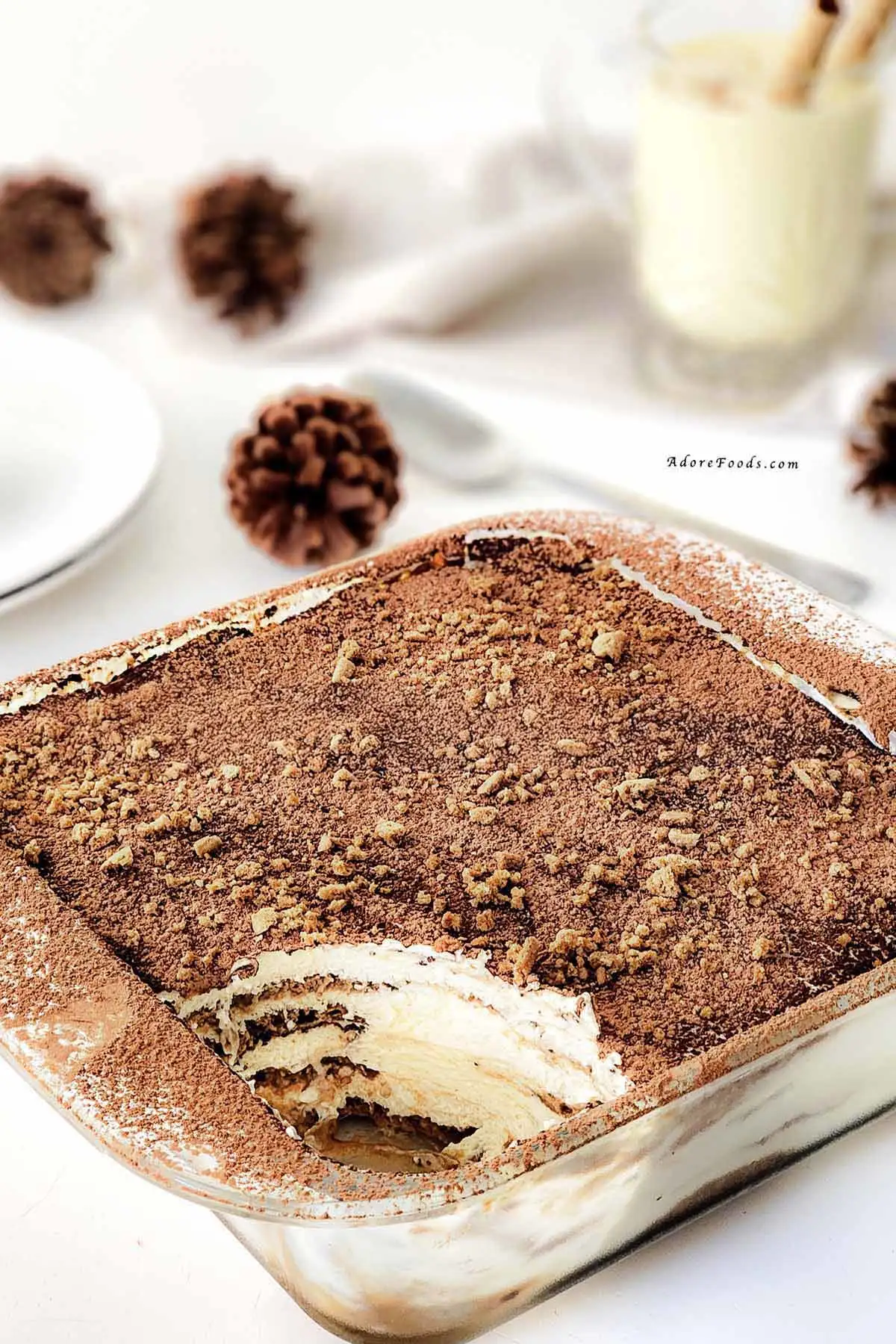 Homemade gingerbread tiramisu in a clear Pyrex baking dish, showing visible layers of dipped gingerbread cookies and creamy mascarpone eggnog filling, topped with a dusting of cocoa powder and crushed gingerbread crumbs, chilled and ready to serve as a festive Christmas dessert.