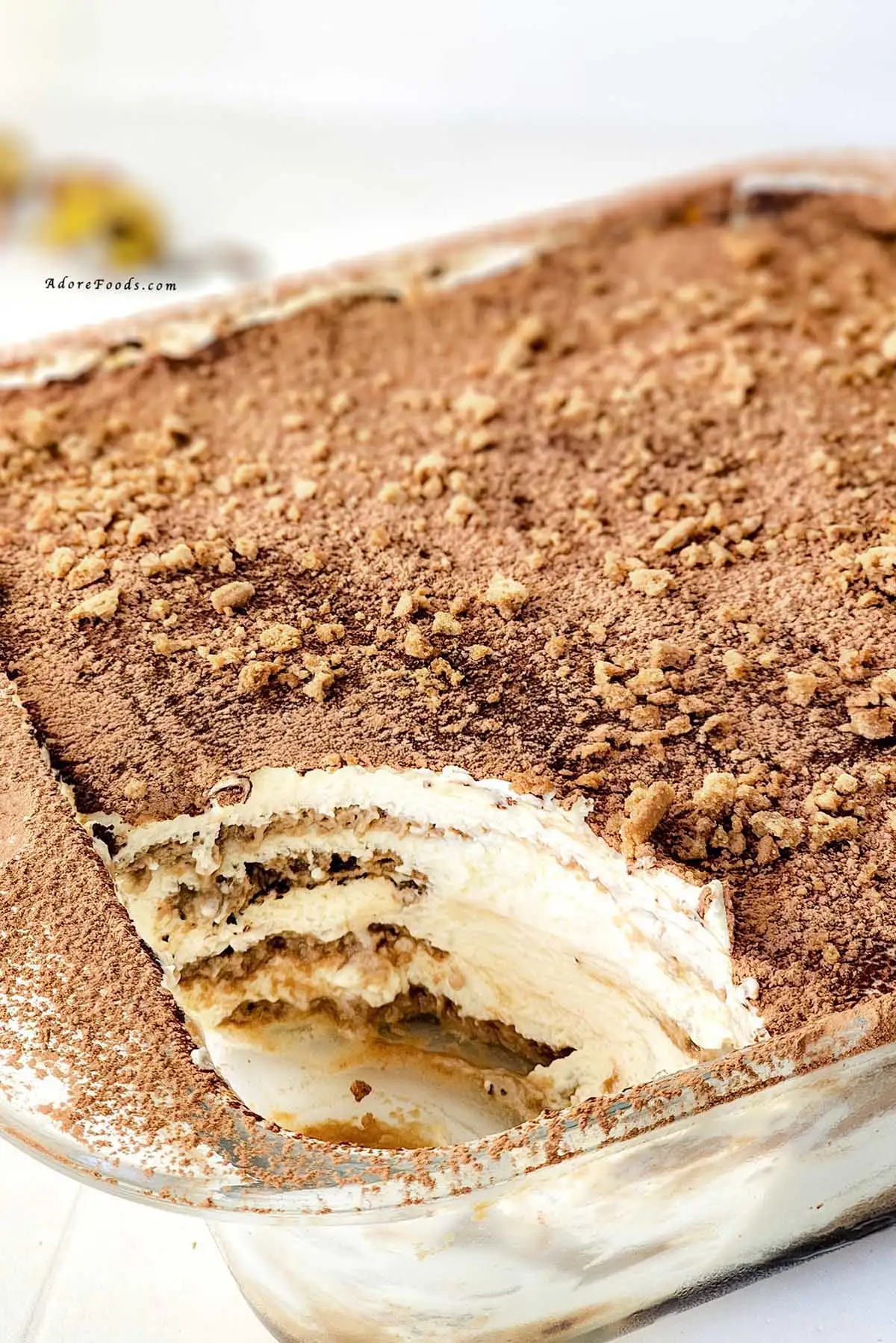 Homemade gingerbread tiramisu in a clear Pyrex baking dish, showing visible layers of dipped gingerbread cookies and creamy mascarpone eggnog filling, topped with a dusting of cocoa powder and crushed gingerbread crumbs, chilled and ready to serve as a festive Christmas dessert.