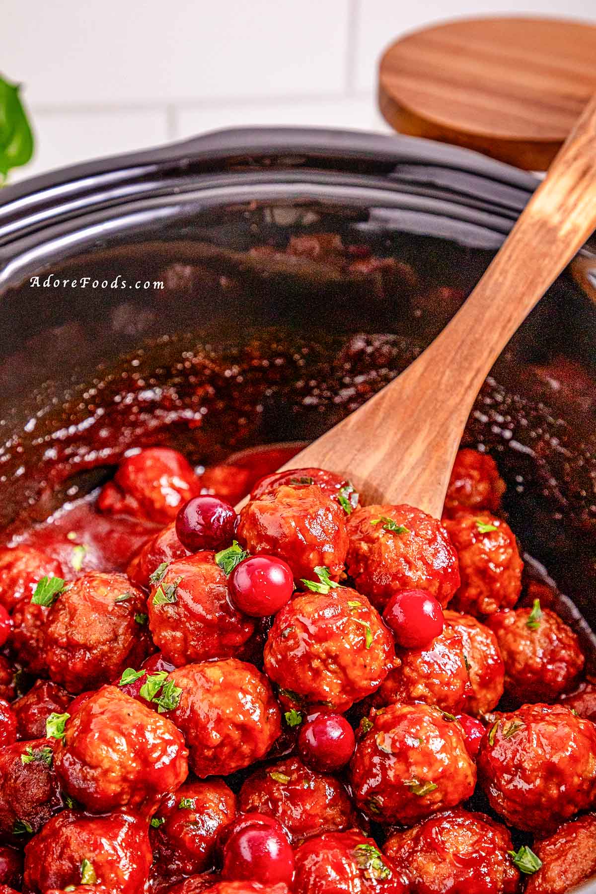 Overhead view of cranberry meatballs cooked in a black slow cooker, coated in a glossy sweet and tangy cranberry sauce and garnished with fresh herbs, ready to serve as an easy holiday appetizer.