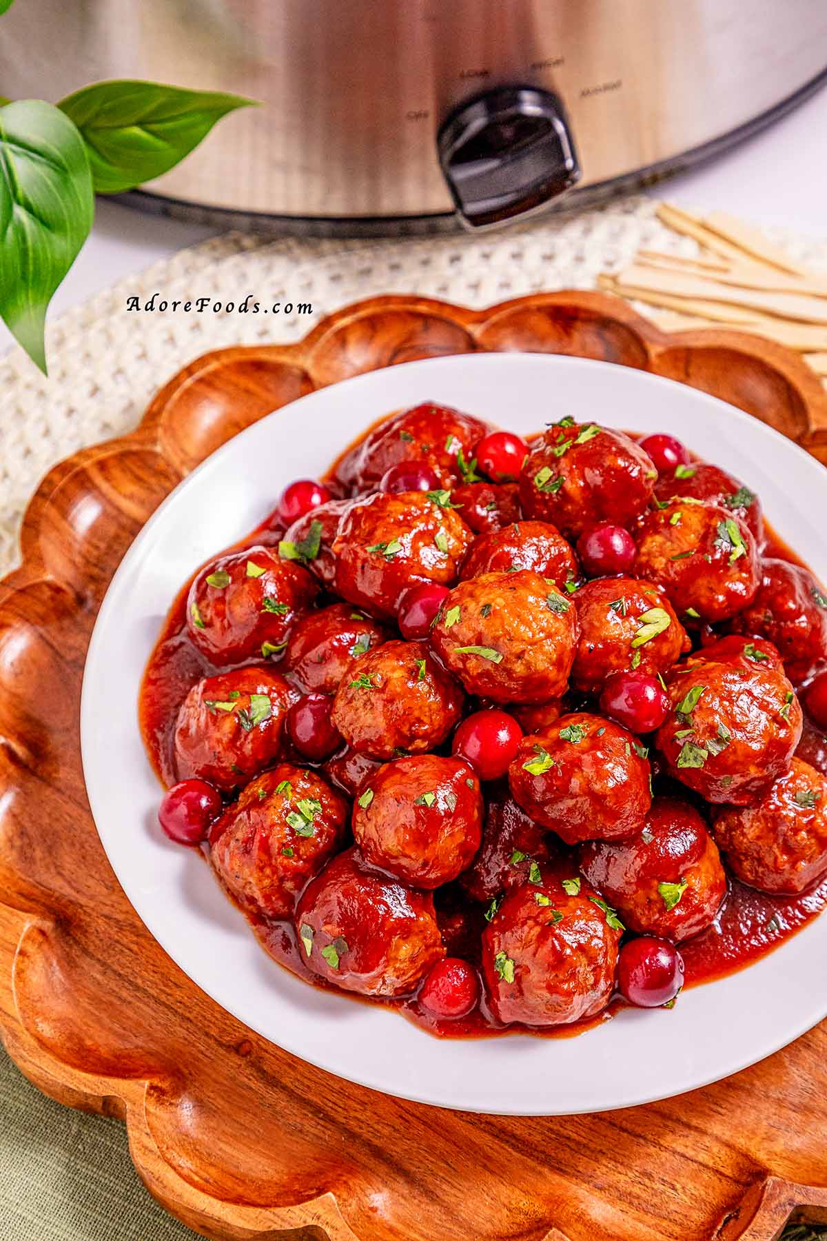 Overhead view of cranberry meatballs cooked on a white plate, coated in a glossy sweet and tangy cranberry sauce and garnished with fresh herbs, ready to serve as an easy holiday appetizer.