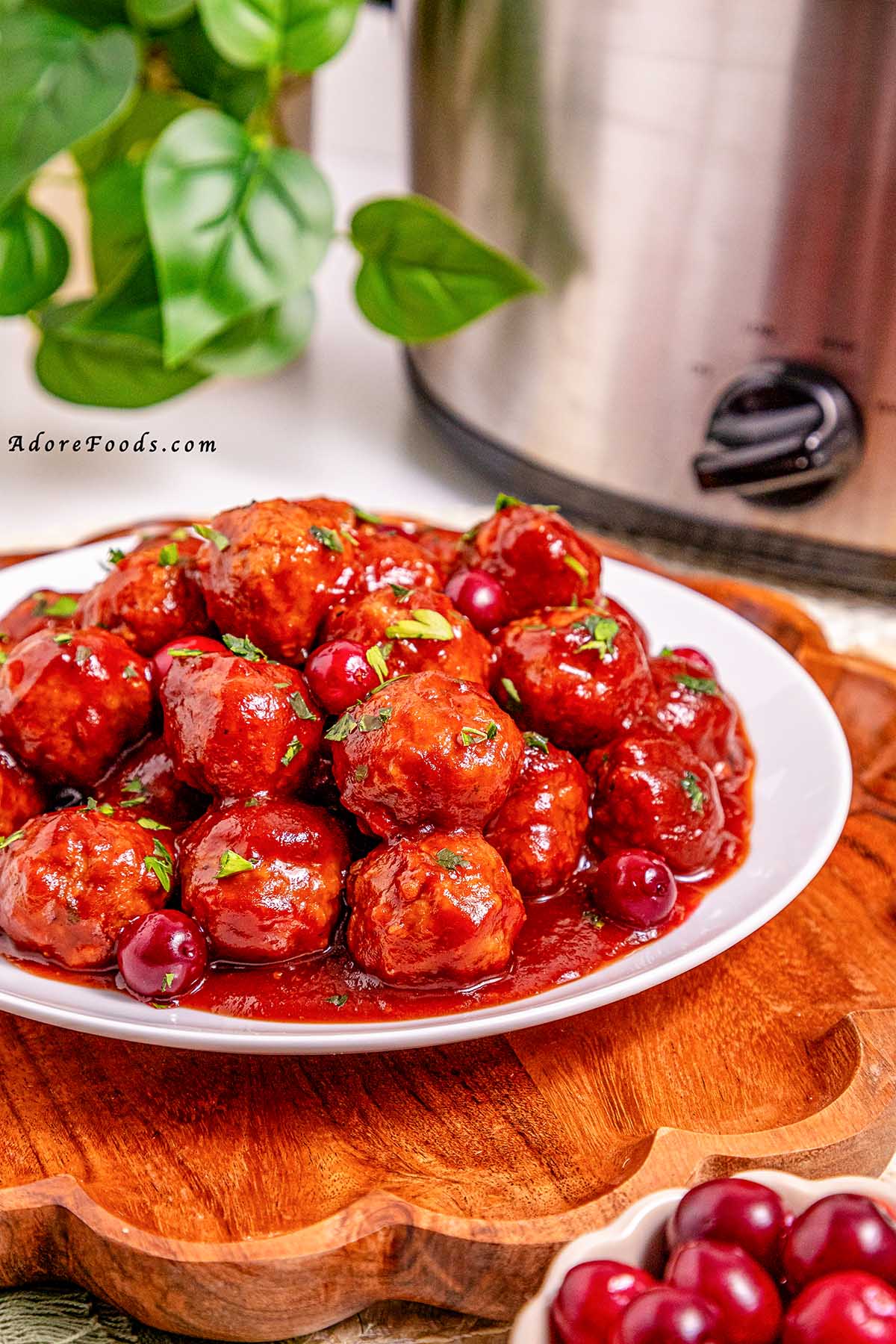 Overhead view of cranberry meatballs cooked on a white plate, coated in a glossy sweet and tangy cranberry sauce and garnished with fresh herbs, ready to serve as an easy holiday appetizer.