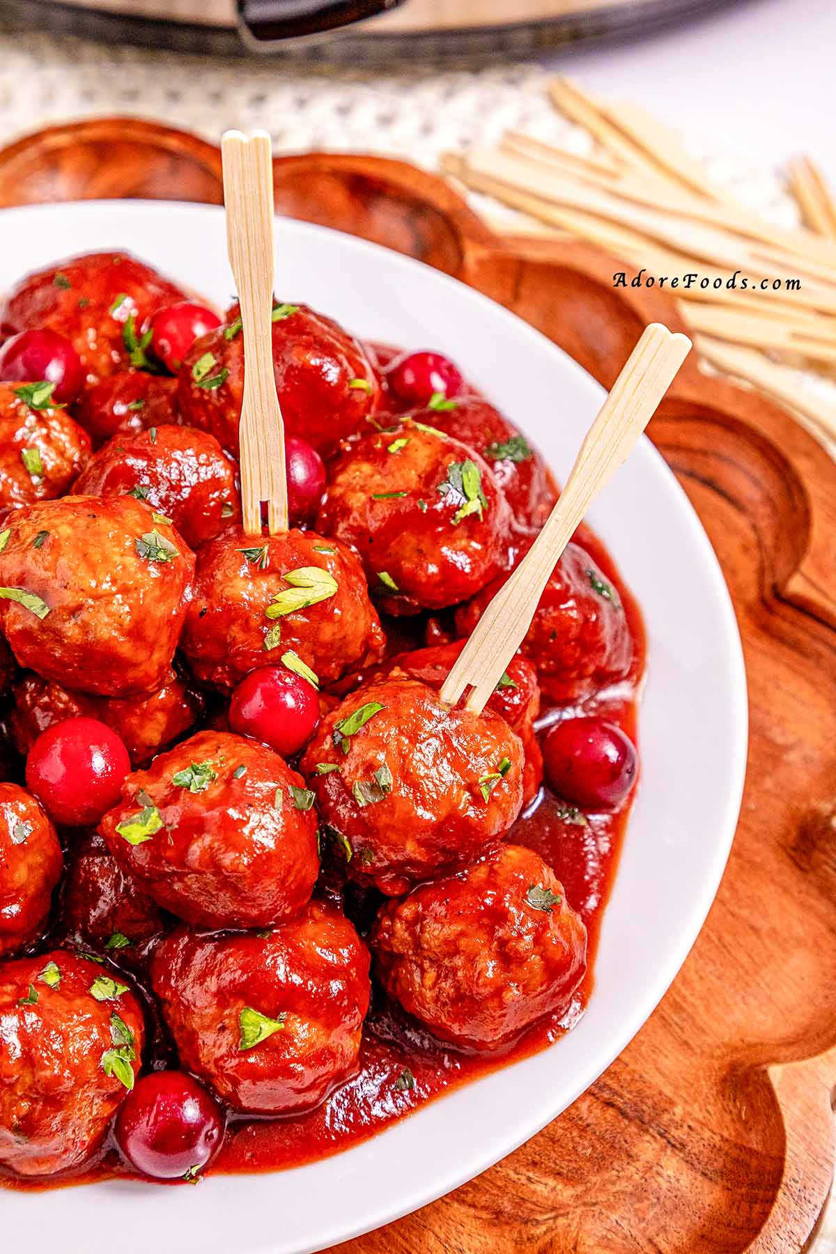 Overhead view of cranberry meatballs cooked on a white plate, coated in a glossy sweet and tangy cranberry sauce and garnished with fresh herbs, ready to serve as an easy holiday appetizer.